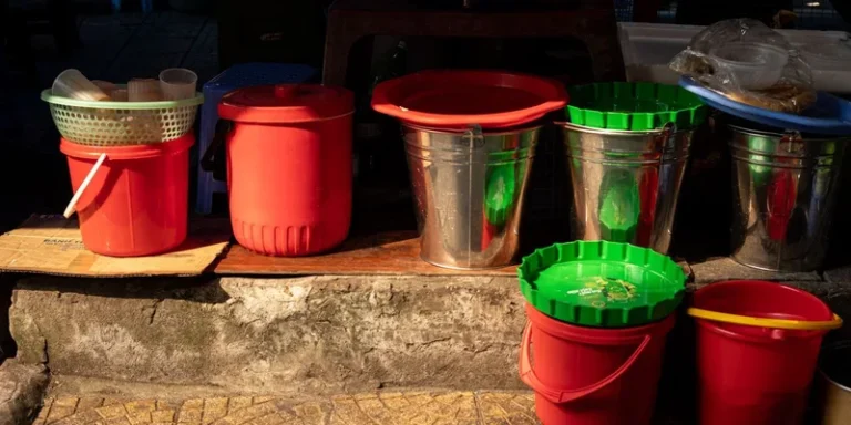 A variety of plastic and metal buckets in sunlight on a stone surface