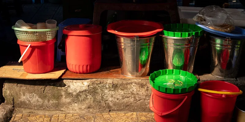 A variety of plastic and metal buckets in sunlight on a stone surface