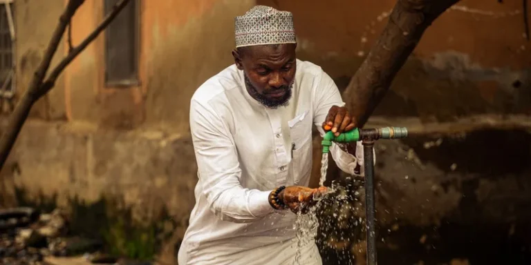 A man washing hands under faucet outdoors in Nigeria, emphasizing hygiene and daily life