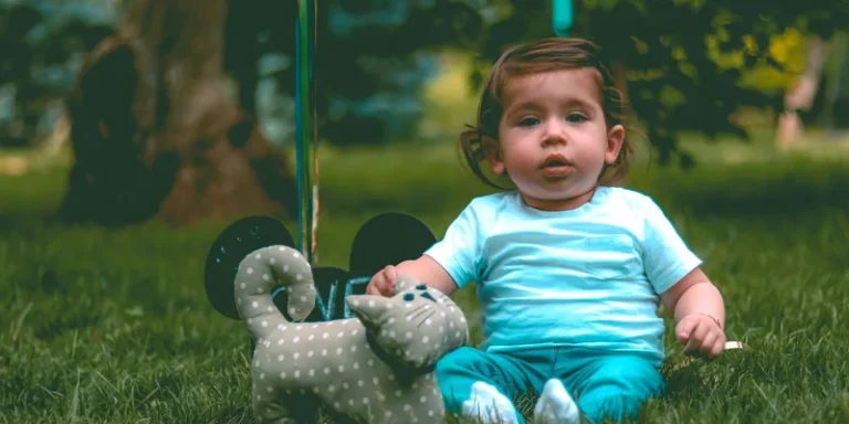 Cute baby sitting on grass with a toy cat in an outdoor park setting