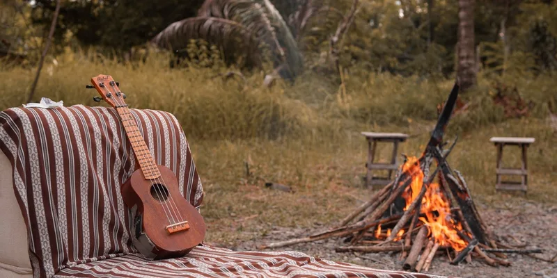 A serene campfire scene with a ukulele and patterned blanket outdoors