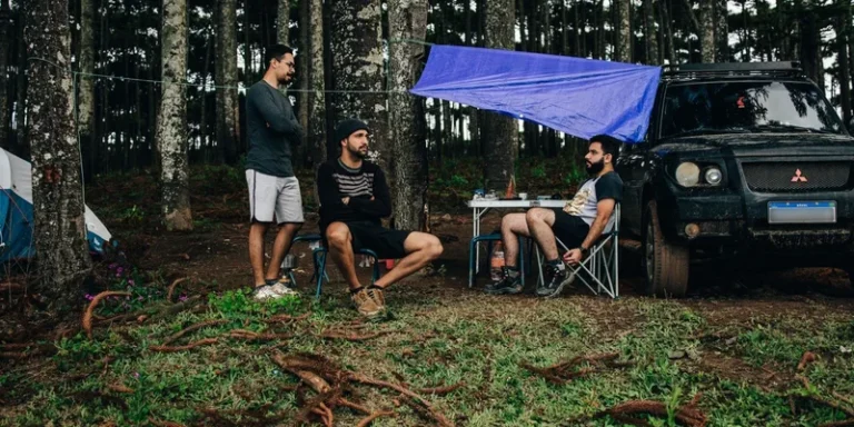 Three men camping in the forest with an SUV, tent, and folding chairs