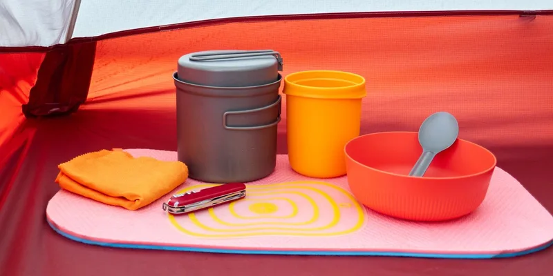Colorful camping cookware and utensils arranged neatly inside a tent