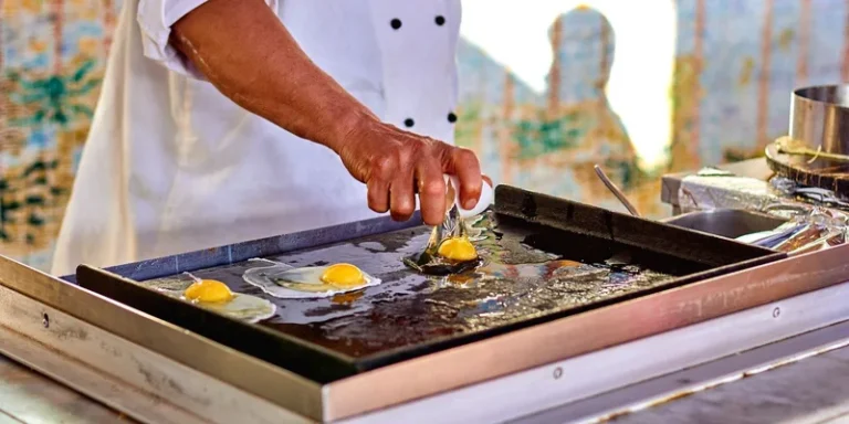 Chef prepares fried eggs on outdoor griddle, emphasizing culinary skill