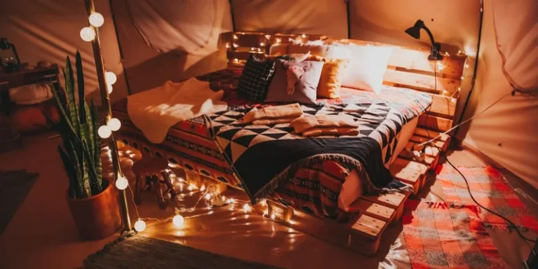 A cozy indoor tent featuring a pallet bed, warm lighting, and decorative pillows for ultimate comfort