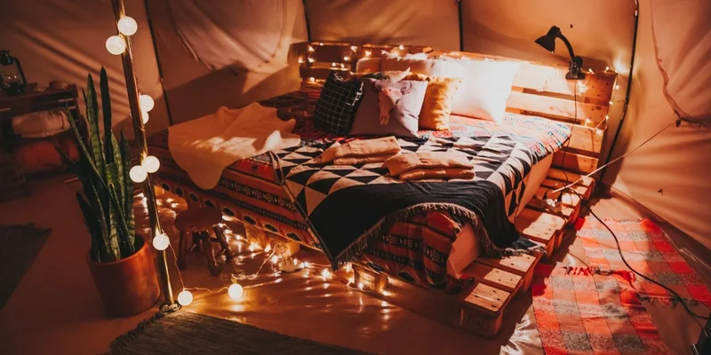 A cozy indoor tent featuring a pallet bed, warm lighting, and decorative pillows for ultimate comfort