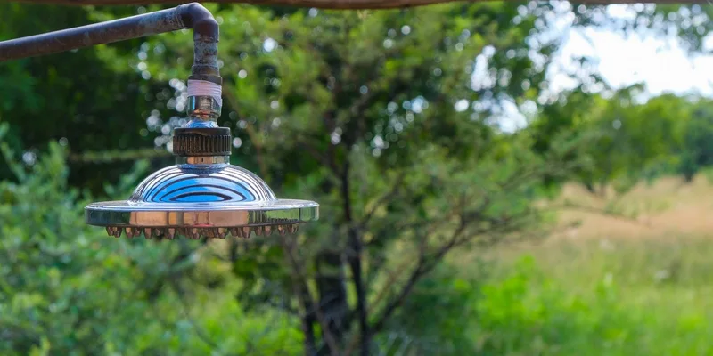 Close-up of a stainless steel shower head outdoors amidst lush green scenery