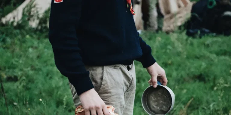 Man in casual wear holding bread and dish, standing outdoors near campsite