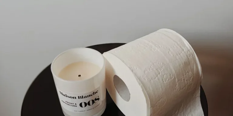 A clean, minimalist setup featuring a scented candle and toilet paper roll on a black surface