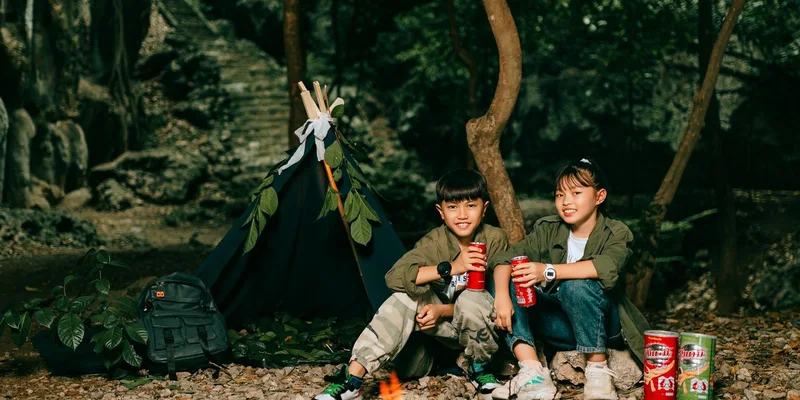 Kids relaxing by a bonfire in a forest campsite, enjoying snacks and nature