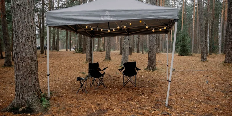 A serene forest campsite with a canopy tent and chairs