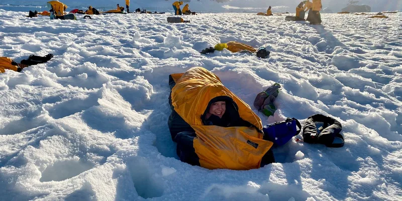 Smiling woman in a sleeping bag during a camping expedition on Antarctica's snowy terrain