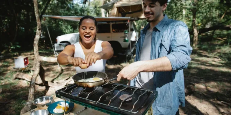A happy couple cooking breakfast on a portable stove at a forest camp, enjoying a sunny day