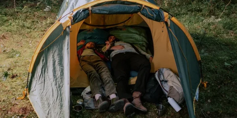 A man and woman lying together in a tent amidst a lush green forest, enjoying a peaceful camping experience