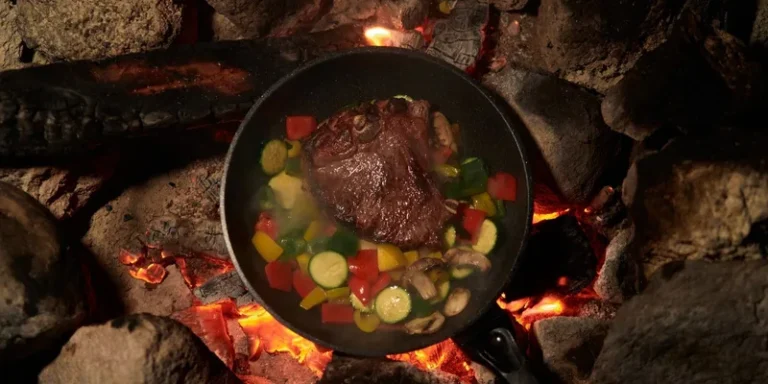 Sizzling beef steak with vegetables cooked over a campfire for an outdoor meal experience