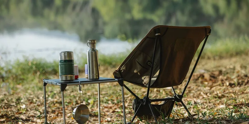 A peaceful lakeside campsite with a folding chair, table, thermoses, and saucepan