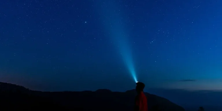Silhouette of a man with headlamp illuminating the starry night sky outdoors