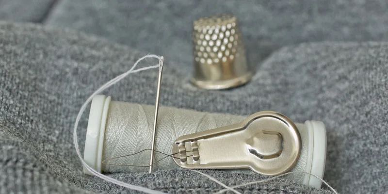 Detailed close-up of sewing essentials including a needle, thread spool, and thimble on grey fabric