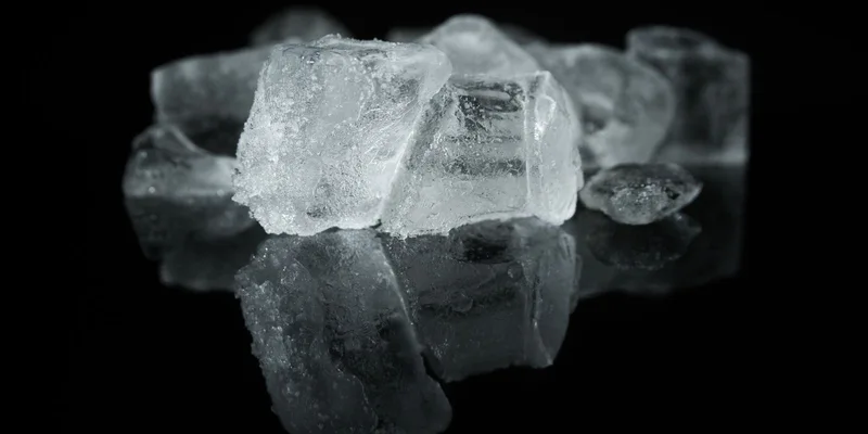 A detailed close-up of ice cubes reflecting on a dark surface