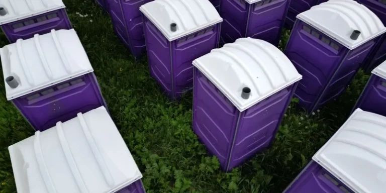 Top-down shot of numerous purple portable toilets arranged outdoors on grass