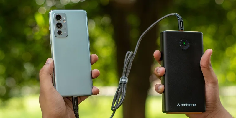 Close-up of hands holding a smartphone connected to a power bank outdoors