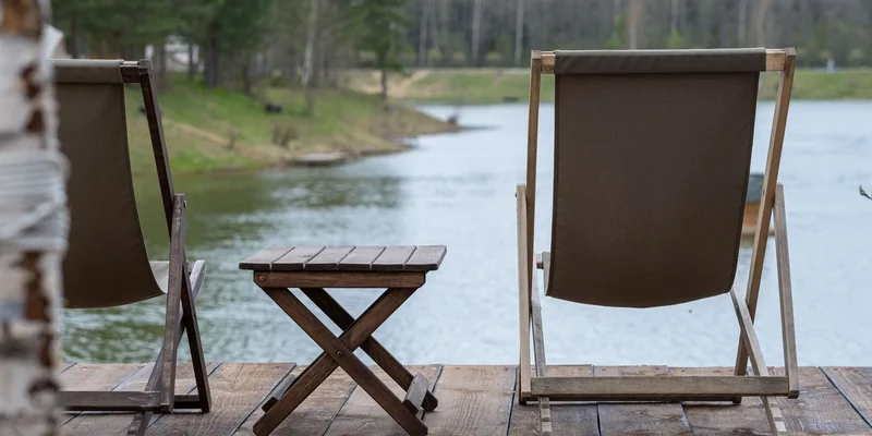 Rustic wooden deck chairs and table overlooking a serene lake and landscape