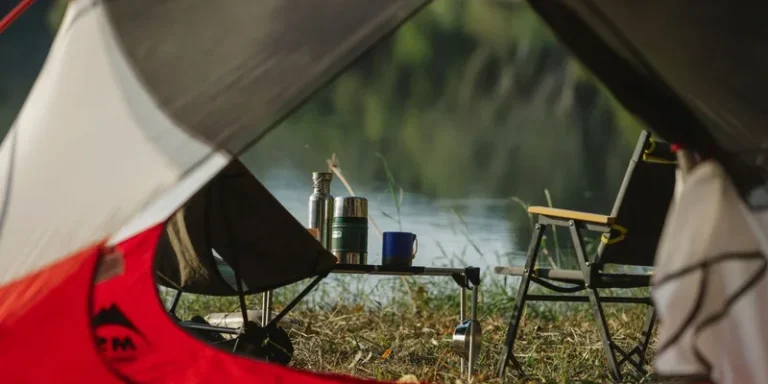 A tranquil view from inside a tent overlooking a lakeside campsite with chair and thermos