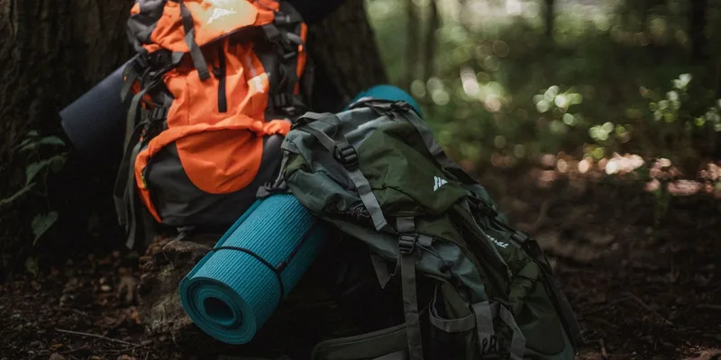 Colorful camping backpacks with mats set against a tranquil forest backdrop