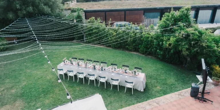 Aerial view of a beautifully set outdoor dinner table with string lights in a lush garden