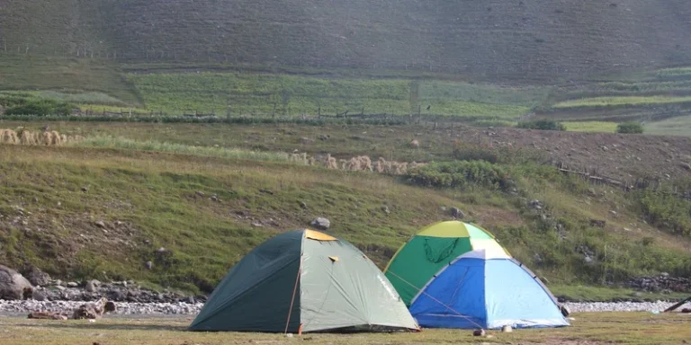 Two tents set on a grassy field against a rolling hillside background