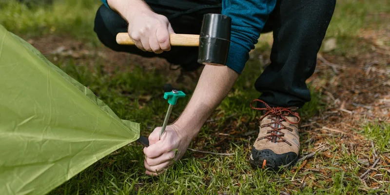 Close-up of a person hammering a tent peg into the ground during a camping trip