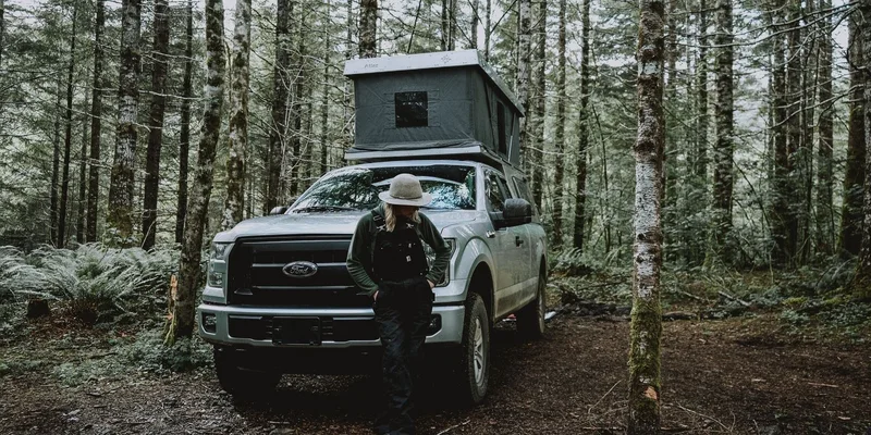 Woman camping with a tent on a pickup truck in the Oregon woods