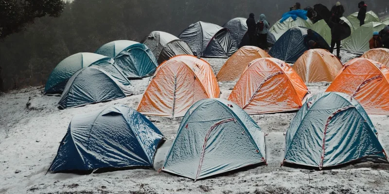 A vibrant campsite with colorful tents in a snowy forest in Singtur Range, India