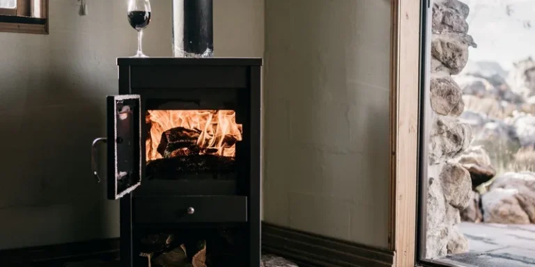 Warm indoor scene with a wood stove burning firewood beside an open door and glass of wine